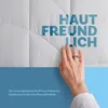 A hand touching a white quilted fabric with German text overlayed. Podgląd zdjęcia produktu