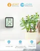 A digital thermometer and hygrometer is shown on a wall next to a potted plant. The display shows temperature and humidity readings. Below the product, there are icons and text indicating different comfort levels (Dry, Comfort, Wet) with corresponding humi Náhľad obrázku produktu