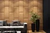 A modern living room with a beige upholstered wall, a gray sofa with pillows, and two black planters with green plants. Produktbild-Vorschau