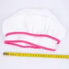 A white chef's hat with pink trim is laid out on a white surface next to a yellow measuring tape. Produktbild-Vorschau