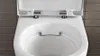 A close-up view of the top of a white toilet bowl with the lid open, set against a tiled wall. Anteprima dell’immagine prodotto