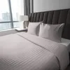 A neatly made bed with striped bedding and pillows in a room with a large window. Anteprima dell’immagine prodotto