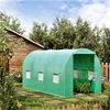 A green greenhouse in a garden setting next to a wooden shed. Produktbild-Vorschau