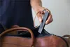 A person is placing a black Invoxia GPS tracker with a tan strap into a brown leather duffel bag. Náhľad obrázku produktu