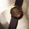 A close-up shot of a Citizen watch with a textured dark brown strap and a multi-colored dial, resting on a textured surface. Produktbild-Vorschau