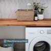 A laundry room scene with a washing machine, a basket, and a plant. Produktbild-Vorschau