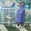 A blue shopping trolley is shown on a wet street with cars and a cyclist in the background. Produktbild-Vorschau