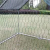 A close-up view of green hexagonal mesh fencing with metal poles visible in the background, set against a blurred grassy area. Voir les images du produit