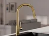 A close-up shot of a modern gold kitchen faucet with a pull-out spout, set against a blurred background of a kitchen or living area. Produktbild-Vorschau