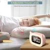 A child is sleeping peacefully in bed, with a pink alarm clock on a wooden nightstand next to them. Musical notes are depicted around the clock and pillow, suggesting it plays melodies. Produktbild-Vorschau