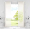 A view of a window with sheer panel curtains, showing a green lawn and trees outside. Produktbild-Vorschau