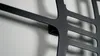 A close-up shot of a black metal wall clock's mounting bracket and part of its frame against a textured white wall. Voir les images du produit