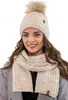 A woman wearing a beige knitted hat with a pom-pom and a matching scarf. Anteprima dell’immagine prodotto