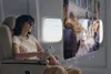 A woman wearing AR glasses is sitting on an airplane seat and holding a device, with a holographic display showing a concert in front of her. Anteprima dell’immagine prodotto