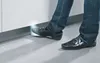 A person's feet wearing black shoes and blue jeans are shown stepping towards a white cabinet with a gray baseboard. Produktbild-Vorschau