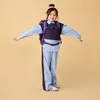 A young girl wearing a backpack and school uniform stands with her arms outstretched against a plain background. Produktbild-Vorschau