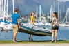 Three people carrying an inflatable boat near a marina. Náhľad obrázku produktu