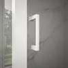 A white shower door handle against a marble-like background, with a view of a garden through a glass door on the left. Anteprima dell’immagine prodotto