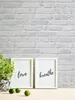 Two framed pictures with inspirational quotes and a potted plant on a wooden surface against a brick wall. Náhled obrázku produktu
