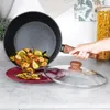 A hand is holding a frying pan filled with paella, pouring it onto a red plate. A glass lid with a wooden handle is nearby. Náhled obrázku produktu