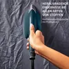 A hand holding a teal steam iron against a wrinkled gray fabric background. Anteprima dell’immagine prodotto