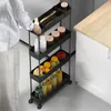A person is reaching for a bottle on a black rolling storage cart filled with food items and kitchen supplies, placed next to a white kitchen cabinet. Produktbild-Vorschau