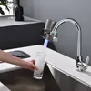 A person is filling a glass with filtered water from a faucet attachment in a modern kitchen. Produktbild-Vorschau