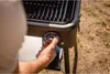 A person's hand is shown adjusting the control knob on a black and silver grill. Náhľad obrázku produktu