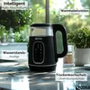 A black electric kettle with a glass top is displayed on a marble countertop, with greenery in the background. Text overlays highlight product features. Produktbild-Vorschau