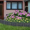 A garden border made of gray, wood-look palisades separates a lawn from a flower bed with pink hydrangeas and yellow roses, in front of a pink house with windows. Voir les images du produit