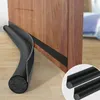 A black foam door draft stopper is shown against a wooden door and floor. Náhled obrázku produktu