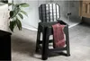 A black plastic stool with a lid and a maroon towel draped over it, placed in a modern bathroom setting. Produktbild-Vorschau