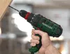 A hand holding a green and black drill, drilling into a wooden beam. Produktbild-Vorschau
