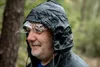 A man wearing a black hooded raincoat in a forest. Produktbild-Vorschau