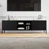 A black TV stand with shelves and doors, placed on a wooden floor in front of a tiled wall and a large TV. Produktbild-Vorschau