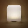 A white cube-shaped lamp with a light source inside, casting a warm glow. Produktbild-Vorschau