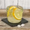A glass jar filled with lemonade and lemon slices, placed on a slate coaster on a wooden surface. Podgląd zdjęcia produktu