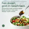 A salad is being dressed with oil from a spoon. Produktbild-Vorschau