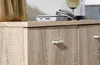 A close-up view of a wooden cabinet with two drawers, showing the handles and the wood grain texture. A white electronic device and a silver bracelet are placed on top of the cabinet. Náhled obrázku produktu