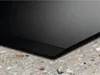 A close-up view of the edge of a black induction cooktop resting on a speckled countertop. Voir les images du produit