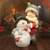 A festive Christmas scene with a snowman and a girl figurine in front of a fireplace. Produktbild-Vorschau