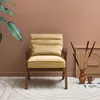 A camel-colored velvet armchair is placed in a room with a brown wall and a patterned rug. Produktbild-Vorschau