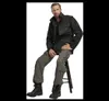 A man is sitting on a stool wearing outdoor pants and a jacket. Anteprima dell’immagine prodotto