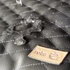 Water droplets on a quilted black surface with a tan brand tag. Produktbild-Vorschau