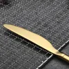 A close-up of a gold-colored knife with a serrated edge resting on a metal mesh grill. Anteprima dell’immagine prodotto