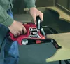 A person is using a red and black belt sander on a wooden furniture piece. Anteprima dell’immagine prodotto