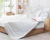A neatly made bed with white bedding, pillows, and a duvet, set in a bright room with a large window. Anteprima dell’immagine prodotto