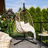 A hanging chair on a balcony with plants and a small table. Produktbild-Vorschau