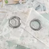 Close-up of two grommets on a sheer curtain with a floral pattern. Produktbild-Vorschau