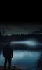 A person stands on the shore of a lake at night, looking out at the water. Podgląd zdjęcia produktu